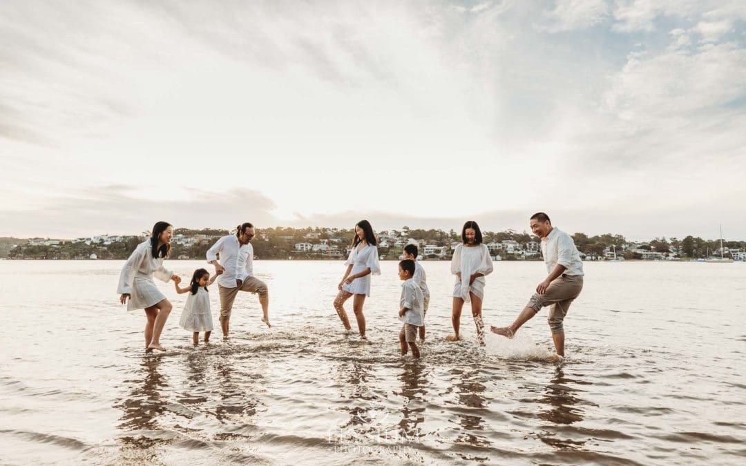 A large family group kick water at each other on a beach at sunset