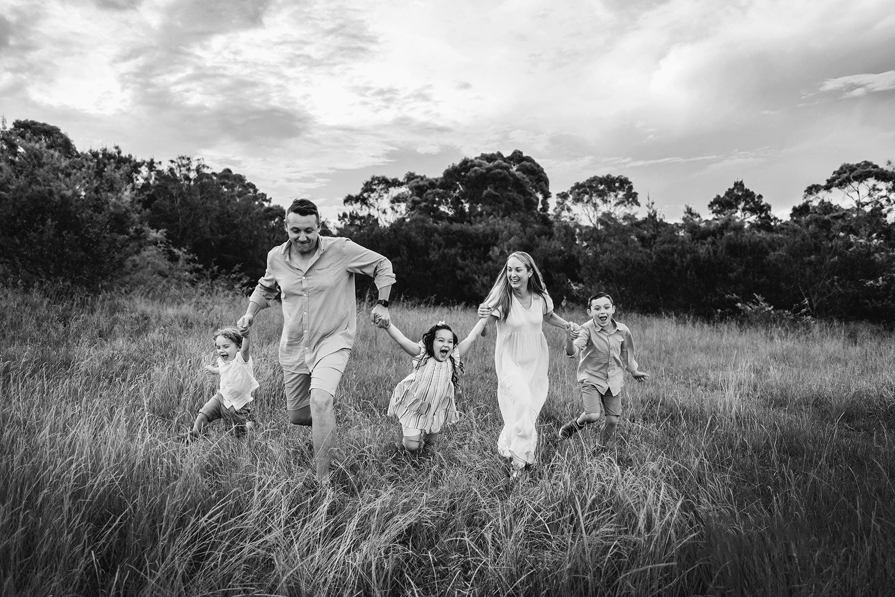 Parents run with their kids through a grassy field at sunset