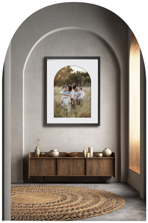 A timber framed family portrait hangs on a wall beside a bright window above a hall table