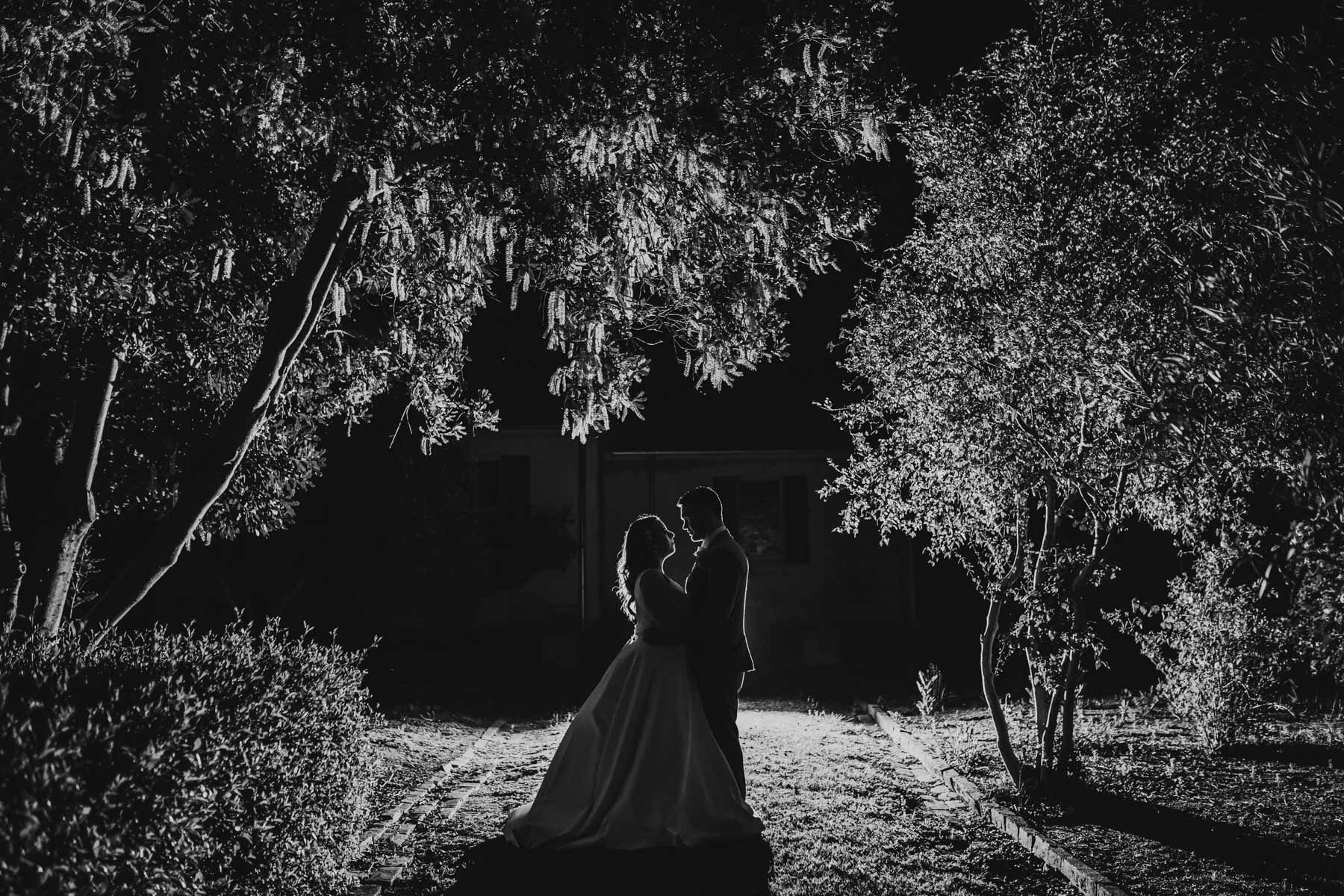 Black and white image of a bride and groom hugging at night surrounded by trees at Gledswood