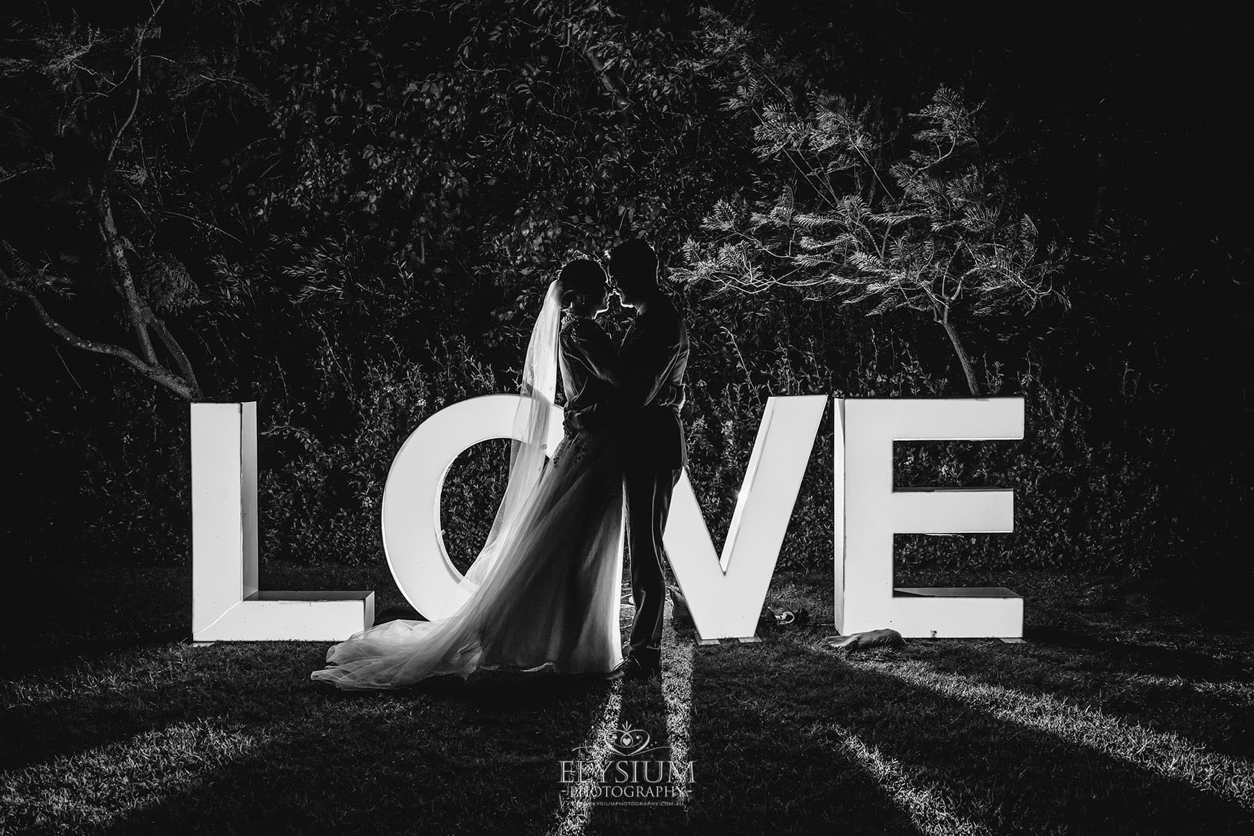 BW-Elysium-Photography-Macarthur-Wedding-Photographer-A&R-578 A bride and groom sit on a log as the sun sets over Burnham Grove