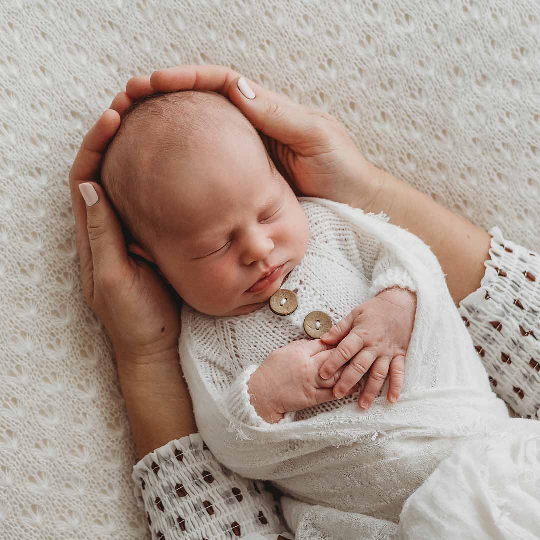 Elysium-Photography-Sydney-Newborn-Photographer-Oakley-72 A mother holds her newborn baby in her hands as she lays wrapped on a white blanket