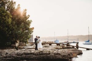 Sydney Wedding Photographer - bride and groom stand on beach rocks at sunset