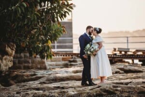 Sydney Wedding Photographer - bride and groom stand on beach rocks at sunset