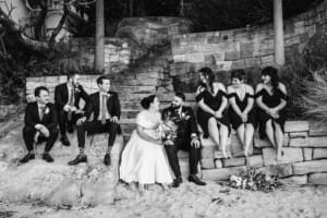 Sydney Wedding Photographer - bridal party sit on a sandstone wall laughing