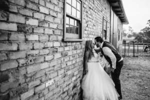 Gledswood Wedding - bride and groom kiss standing against a brick wall