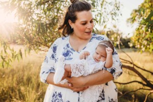 A mother holds her baby girl in a grassy field