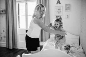 A little girl jumps on her bed holding mum's hands