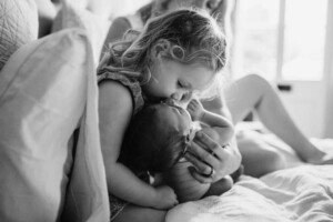 A little girl kisses her newborn brother's head