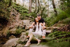 A woman sits in her fiancee's lap and hugs his legs