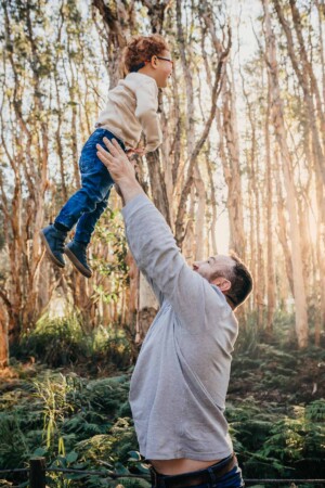 A father hoists his little boy in the air as he soars above his head