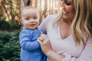A baby girl smiles at the camera while being held by her mum