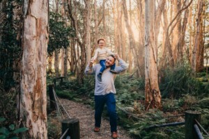 A little boy rides on his dads shoulders running along a path