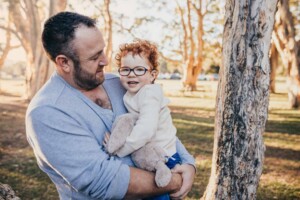 A dad cuddles his little boy as the sun sets behind them