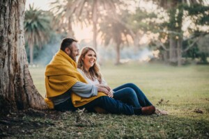 Parents cuddle under a blanket in a Sydney park photo shoot