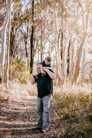 A dad carries his little boy on his shoulders as they giggle together