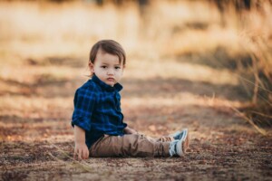 A little boy sits in the middle of a dusty path at sunset