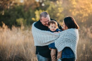 Parents snuggles their son wrapped in a blanket at sunset