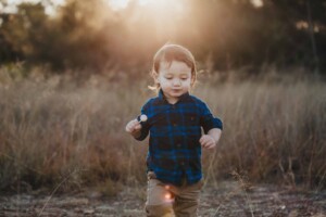 A little boy crosses a grass field eating a lollypop as the sun sets behind him