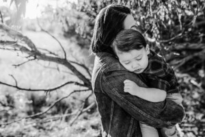 A little boy rests on his mums shoulder with the sun setting behind them