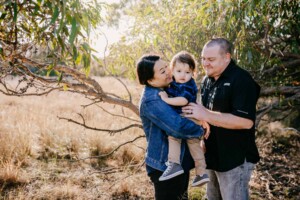 Parents hold their baby boy between them in a grassy field