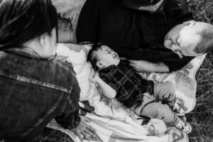A tickles his son as they lay together on a rug in a grassy field