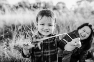 A little boy tries to tickle his photographer with a piece of grass