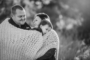 A little boy rests his head on his mum's shoulder as they snuggle in a blanket