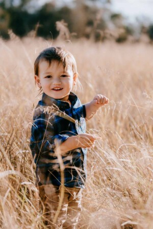 A little boy smiles as long grass tickles his face at sunset