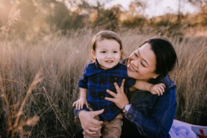A mother snuggles her son in the long grass at sunset