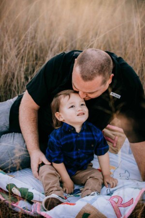 A father snuggles his son in the long grass at sunset