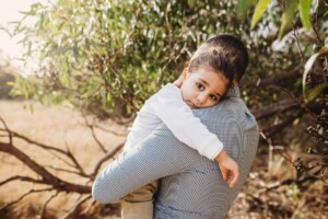 A father and son share a cuddle under a tree during a photo session