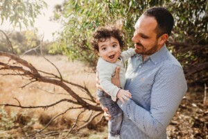 A father and son share a cuddle under a tree during a photo session