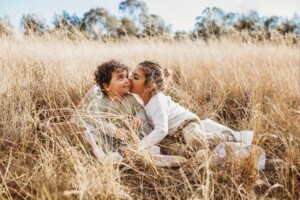 A boy kisses his brothers cheek as they sit in a grass field at sunset