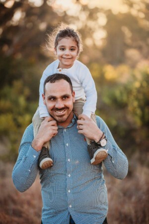 A father holds his son's hands as the little boy sits high on daddy's shoulders
