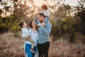 A family laugh together with their 2 little boys as the sun sets behind them