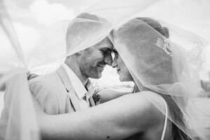 A bride and groom snuggle under the brides veil after their wedding