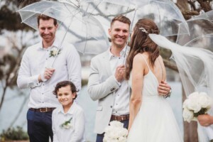 A bride & groom shelter under umbrellas during their wedding