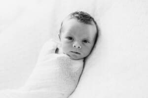 A newborn baby lays wrapped in white on a textured blanket