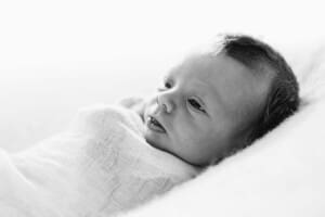 Profile of a newborn baby's face in a white wrap with a bright window behind him