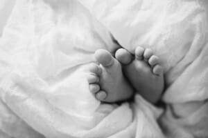 Tiny newborn toes poke out from a white linen wrap, black and white photograph
