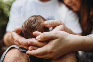 Parents hands hold their tiny newborn's head showing his soft hair and how small he is