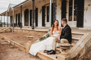 Gledswood Wedding - A bride and groom laugh together, sitting on the steps of Gledswood estate homestead