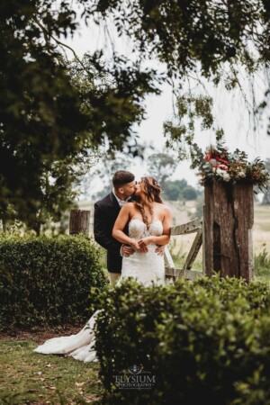 Gledswood Wedding - Bride and groom share a kiss, standing against a rustic gate at Gledswood Estate