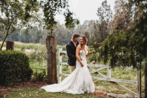 Gledswood Wedding - Bride and groom laugh, standing against a rustic gate at Gledswood Estate