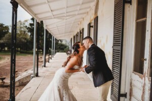 Gledswood Wedding - Bride and groom sharing a kiss, standing on the veranda at Gledswood Homestead