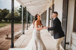 Gledswood Wedding - Bride and groom sharing a laugh, standing on the veranda at Gledswood Homestead