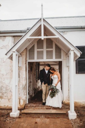 Gledswood Wedding - A groom cuddles his bride under an archway at Gledswood Homestead