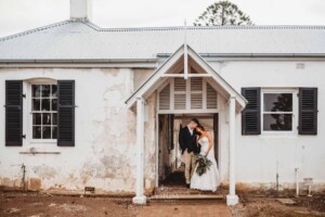 Gledswood Wedding - A groom cuddles his bride under an archway at Gledswood Homestead