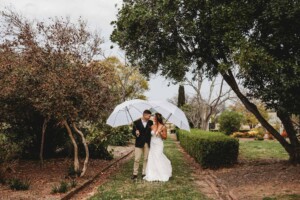 Gledswood Wedding - A bride and groom stand under white umbrellas as it rains on their wedding day